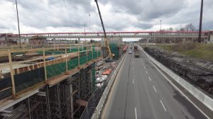 Place d'Orléans O-Train station under construction beside Highway 174, with the red pedestrian bridge to the mall
