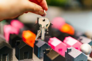 A hand holding house keys above small model houses